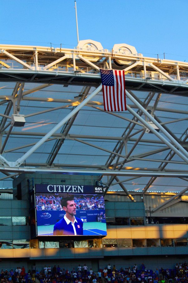 Djokovic being interviewed after he won the match with the American flag hanging above.